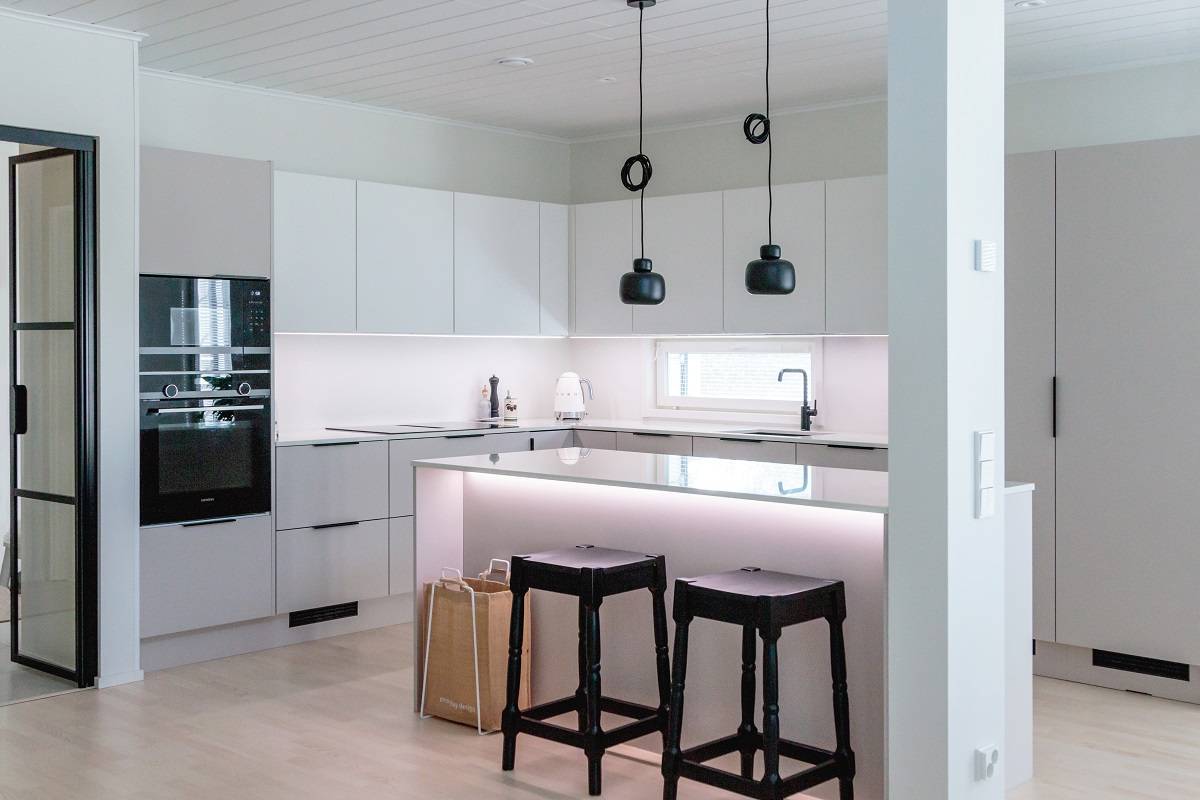 La cocina está iluminada por tiras de LED de longitud completa en un perfil de aluminio, lámparas de techo suspendidas sobre la isla y luz adicional bajo el borde frontal de la isla.